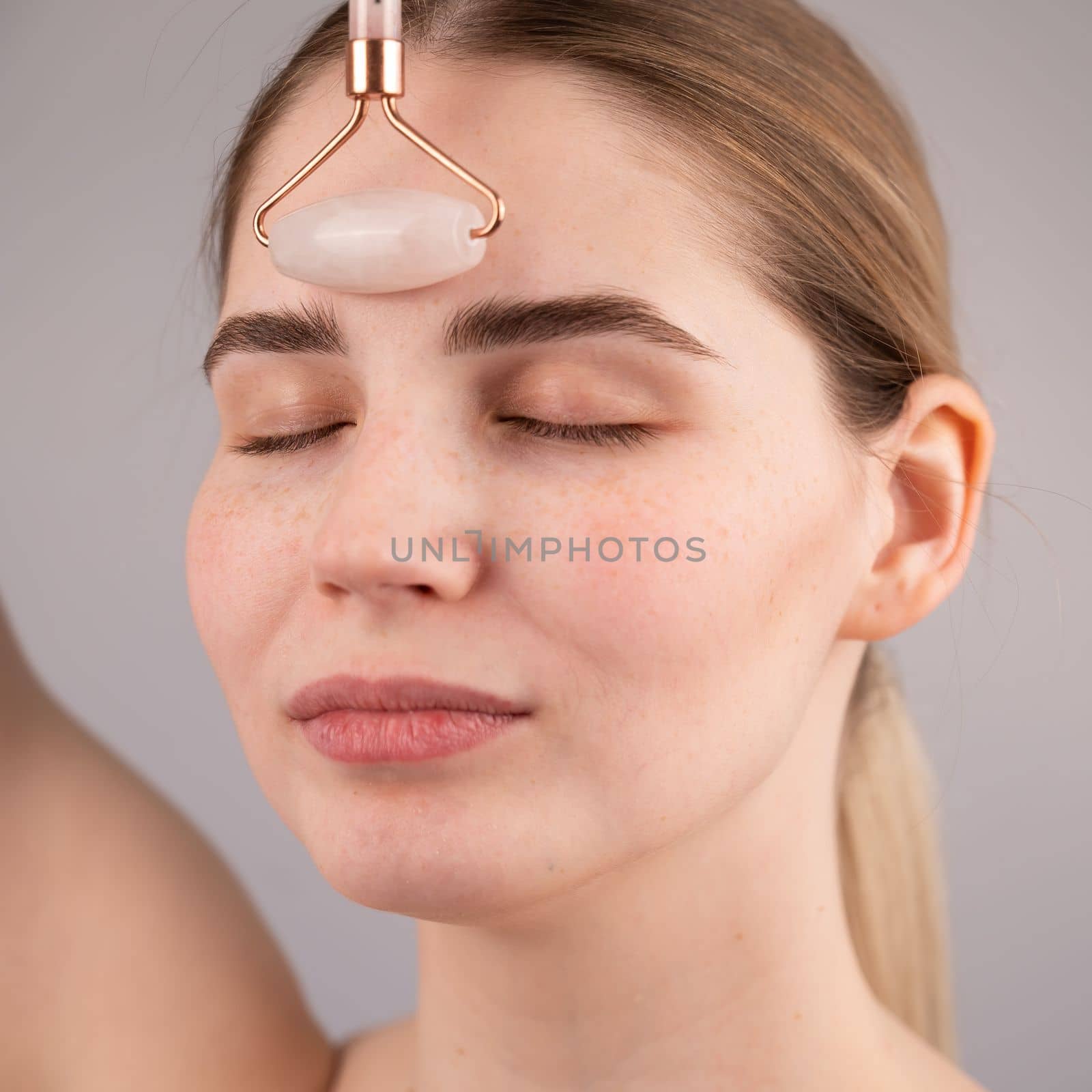 Close-up portrait of a woman uses a quartz roller massager to smooth wrinkles on her forehead. by mrwed54