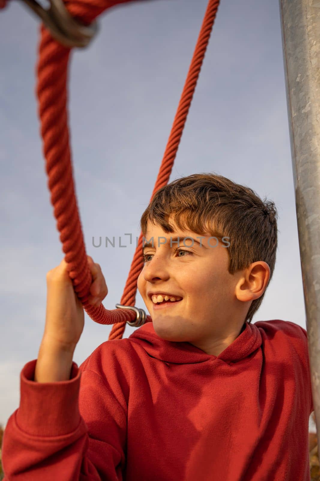 portrait of happy smiling cute boy hanging on a rope at sunset. Positive concept.