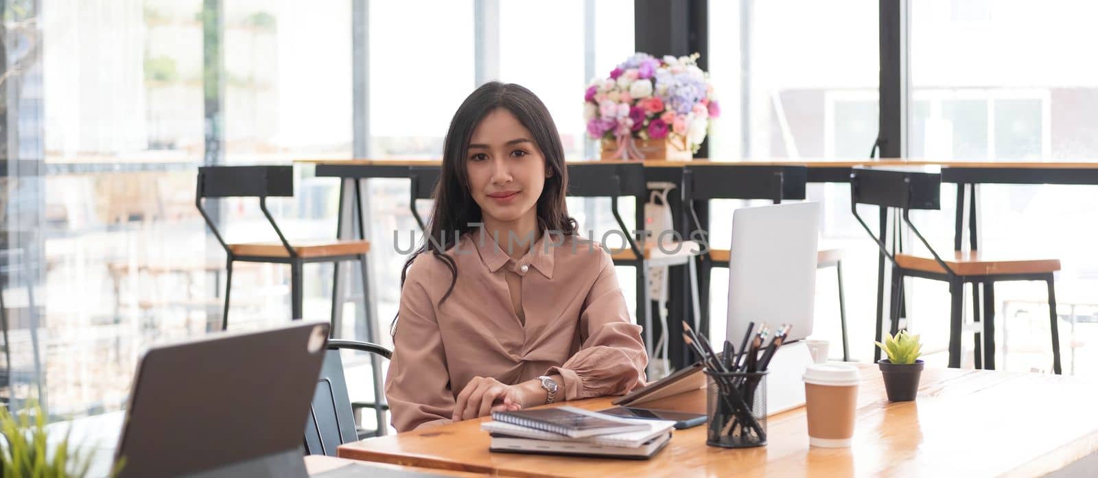 Portrait of a charming Asian business woman working on a laptop in the office. by wichayada