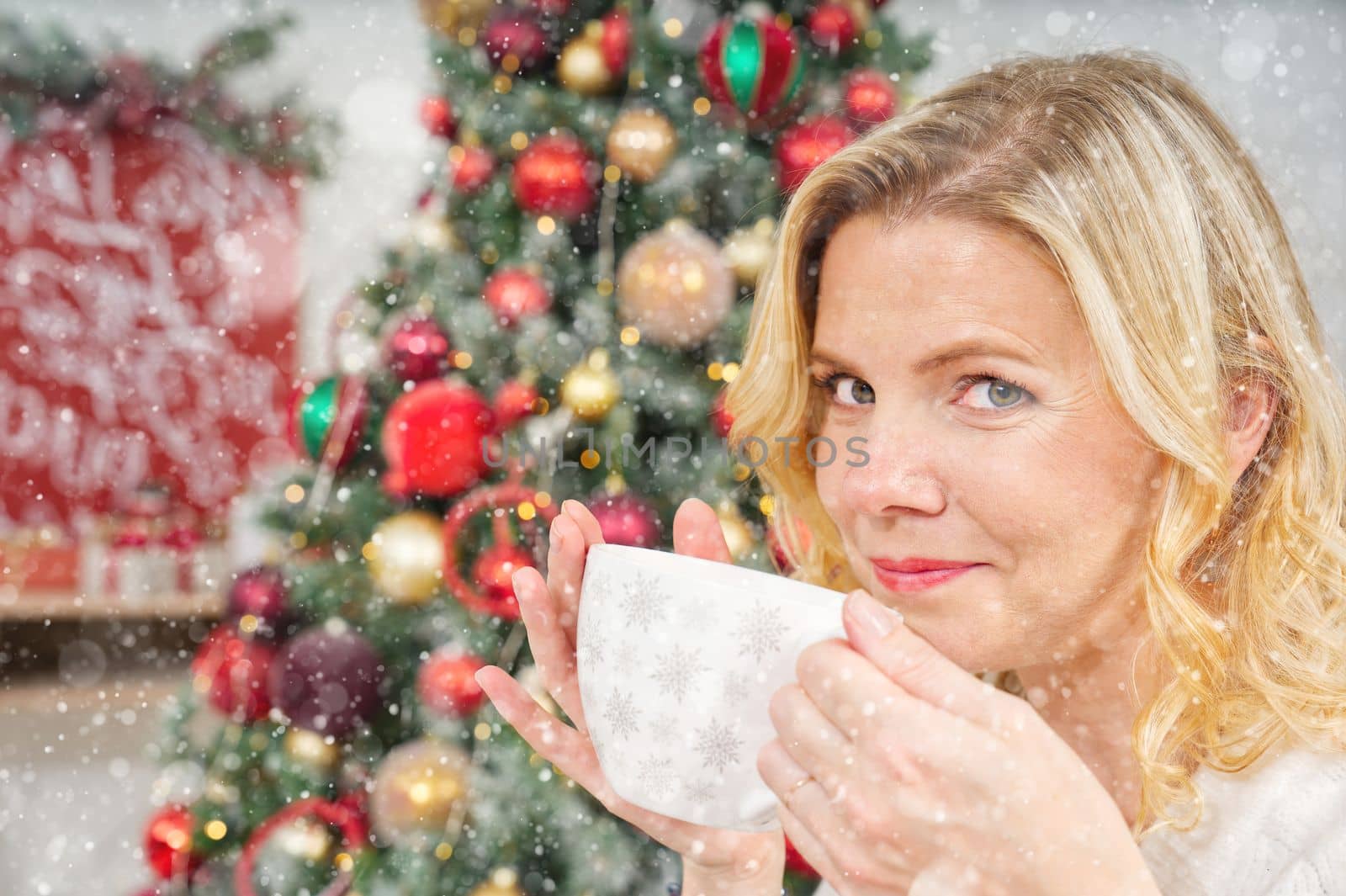 Girl in white sweater holding a cup of warm coffee or tea on background of a Christmas tree. by PhotoTime