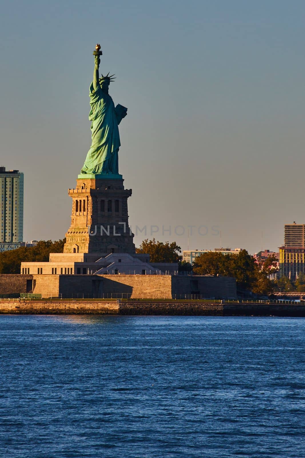 Light filling in half of Statue of Liberty in New York City from waters with golden hues by njproductions