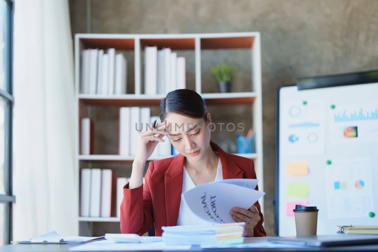 Portrait of a thoughtful Asian businesswoman looking at financial statements and making marketing plans using a computer on her desk.