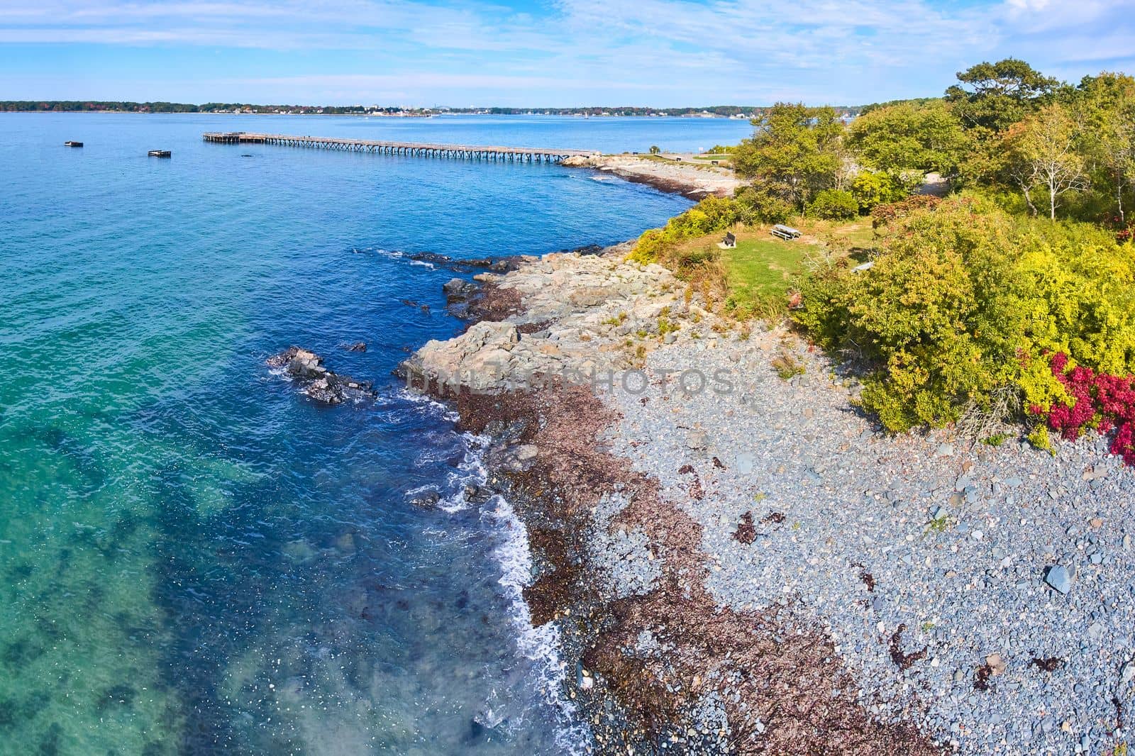 Aerial of blue waters over Maine coastline with forest and pier in background by njproductions