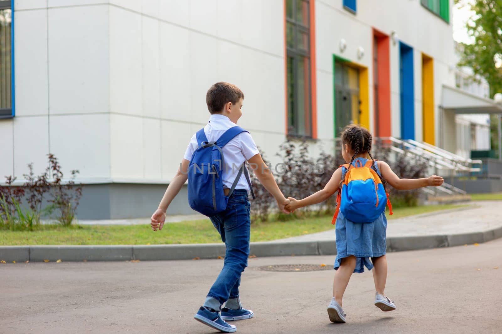 two schoolchildren, a little girl and a boy, brother and sister with backpacks hold hands run to school in the morning on a sunny day. Close up. Mock up