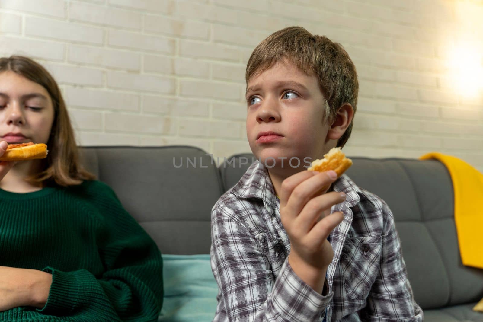 Cute Caucasian preschooler boy is sitting at home on the couch, eating pizza and watching TV. a child alone at home watching cartoons without control