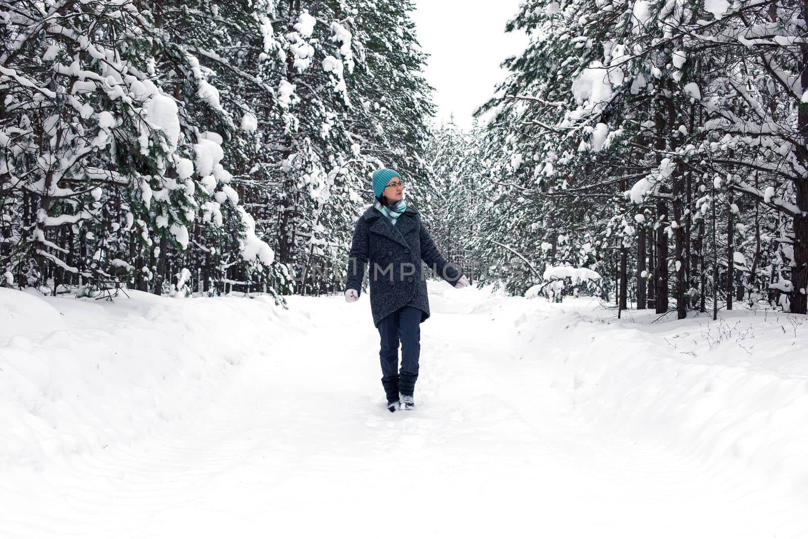 A girl walks through a beautiful winter snowy forest, looks at the trees.