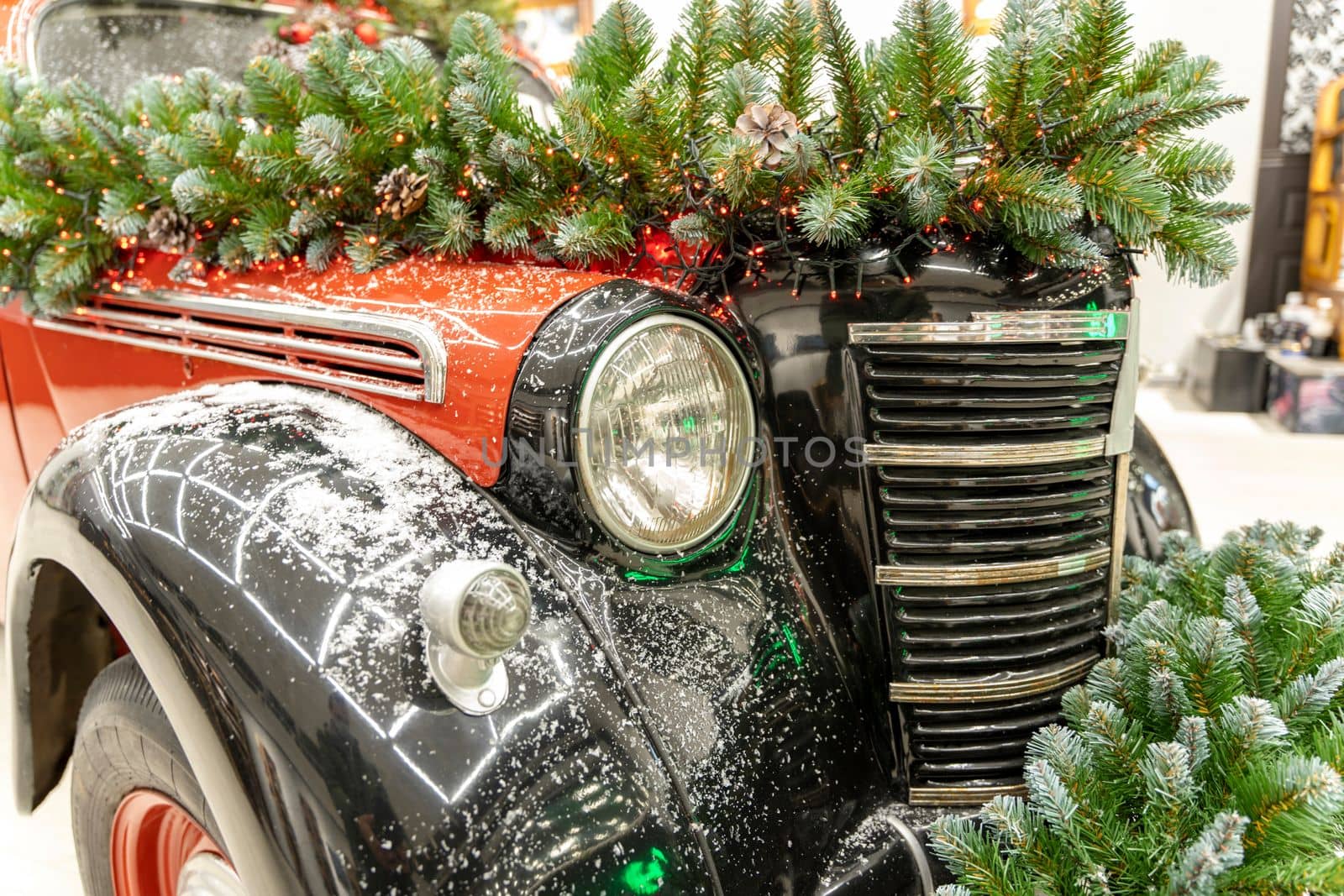 The vintage classic car is decorated with fir branches and Christmas decorations. A beautifully and stylishly decorated car shines with an outfit for Christmas and New Year.