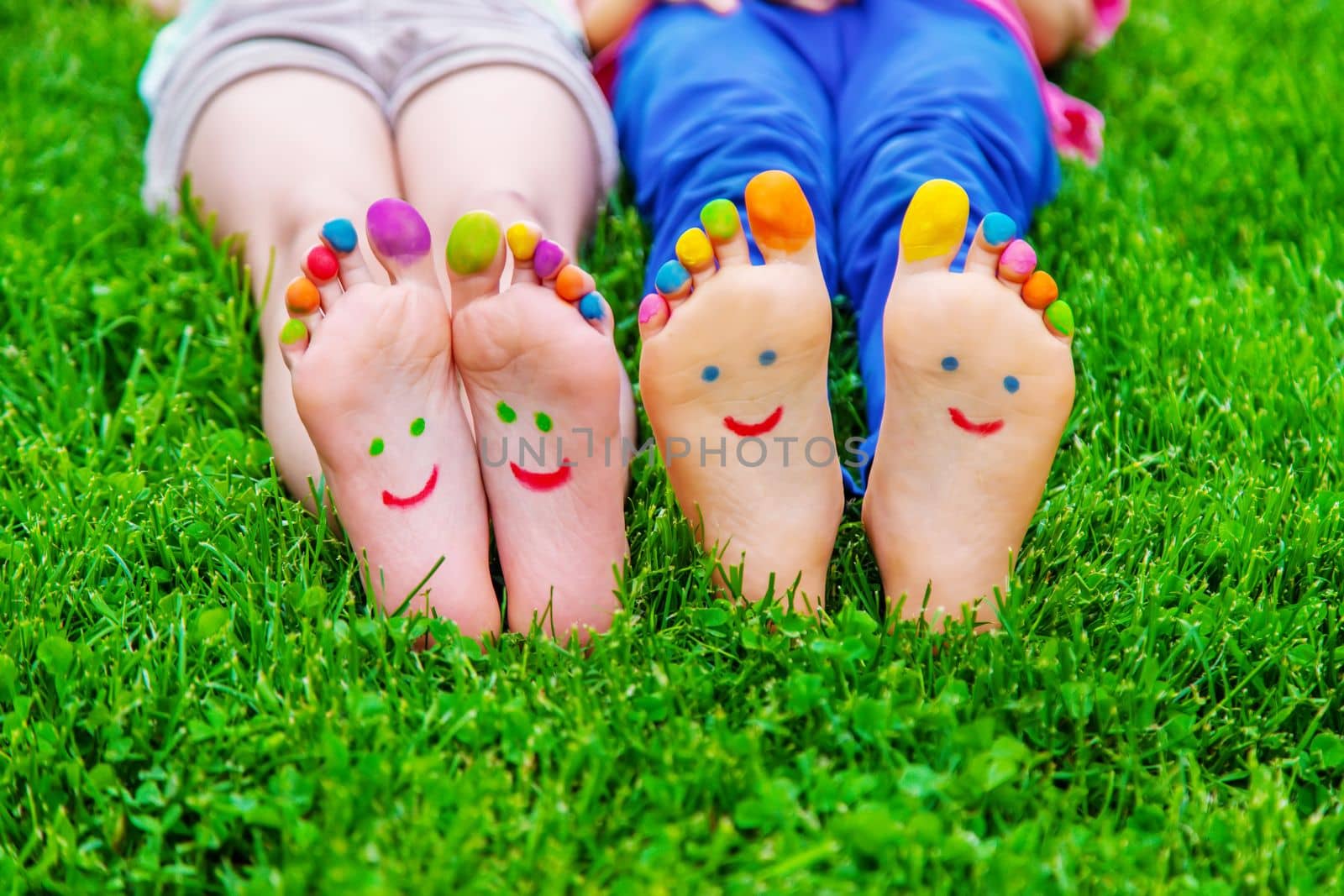 Children's feet with a pattern of paints smile on the green grass. Selective focus. by mila1784