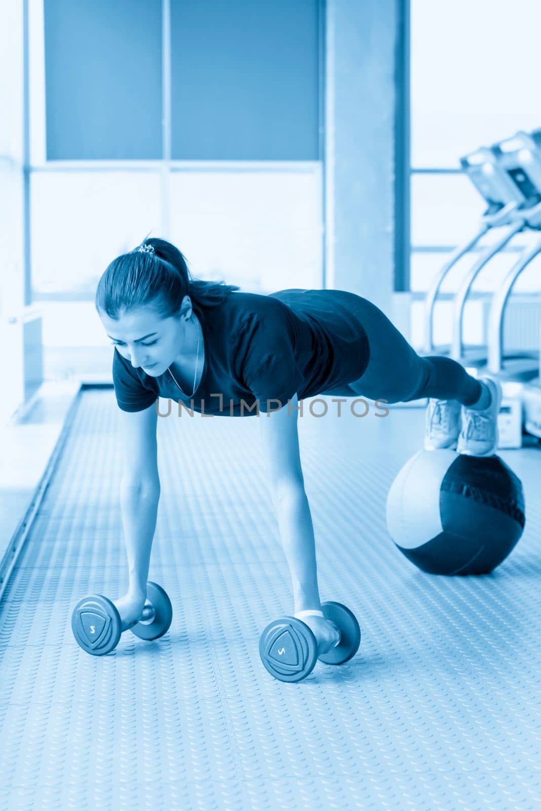 Fitness girl doing dumbbells and medicine ball plank. Woman doing floor workout at gym by Mariakray
