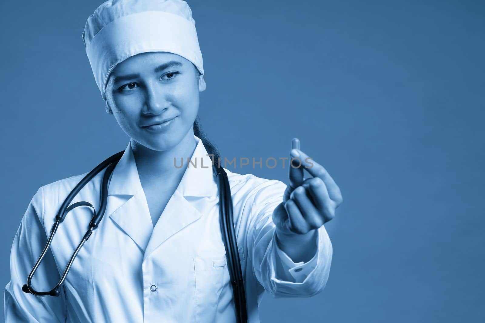 Young female doctor holding a pill, looking at it and giving it as a treatment to the patient by Mariakray