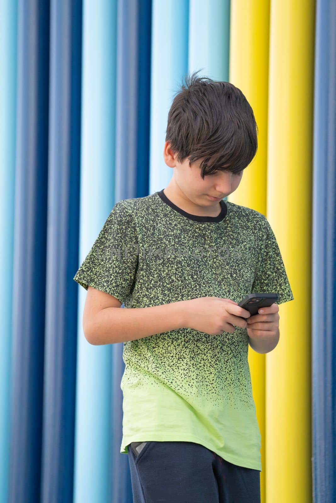 Portrait of a young boy using a smartphone walking on coloured background. Immersed in technology concept
