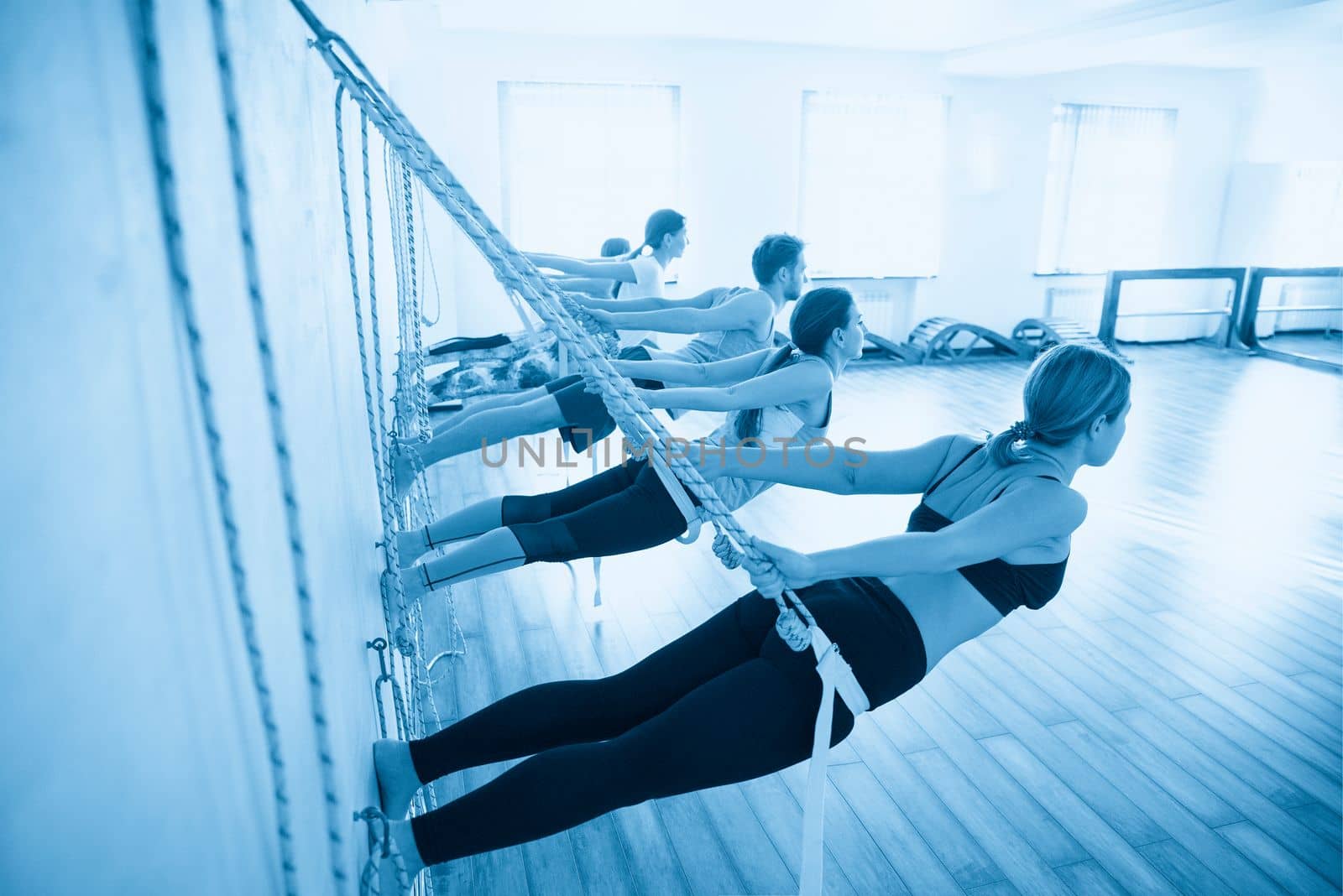 women hanging on ropes upside down practicing yoga on ropes stretching in gym. Fit and wellness lifestyle.