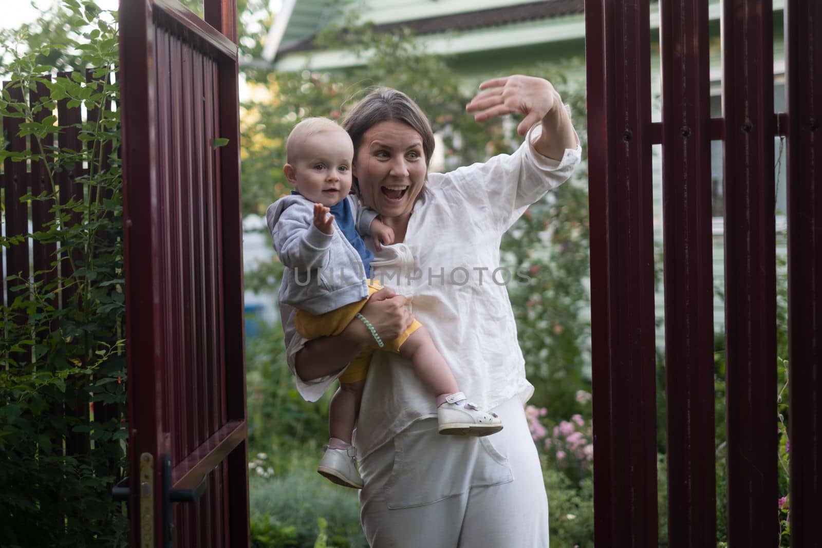 Curious woman with a baby opening the gate of fence and looking at camera welcoming friends