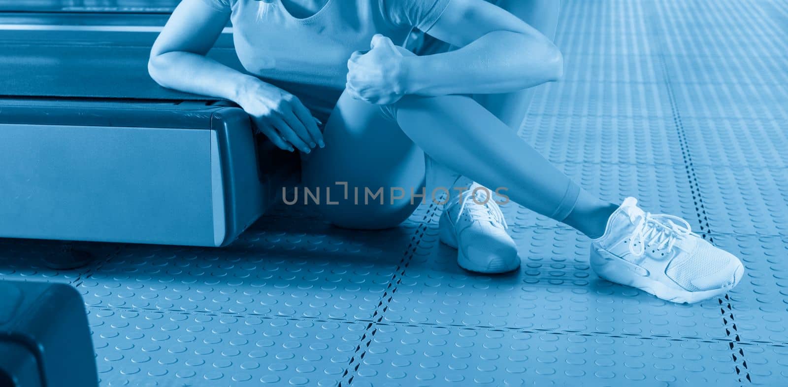 Young woman in sportswear having ache in knee while training in gym, Girl sitting on a floor touching her knee in pain by Mariakray