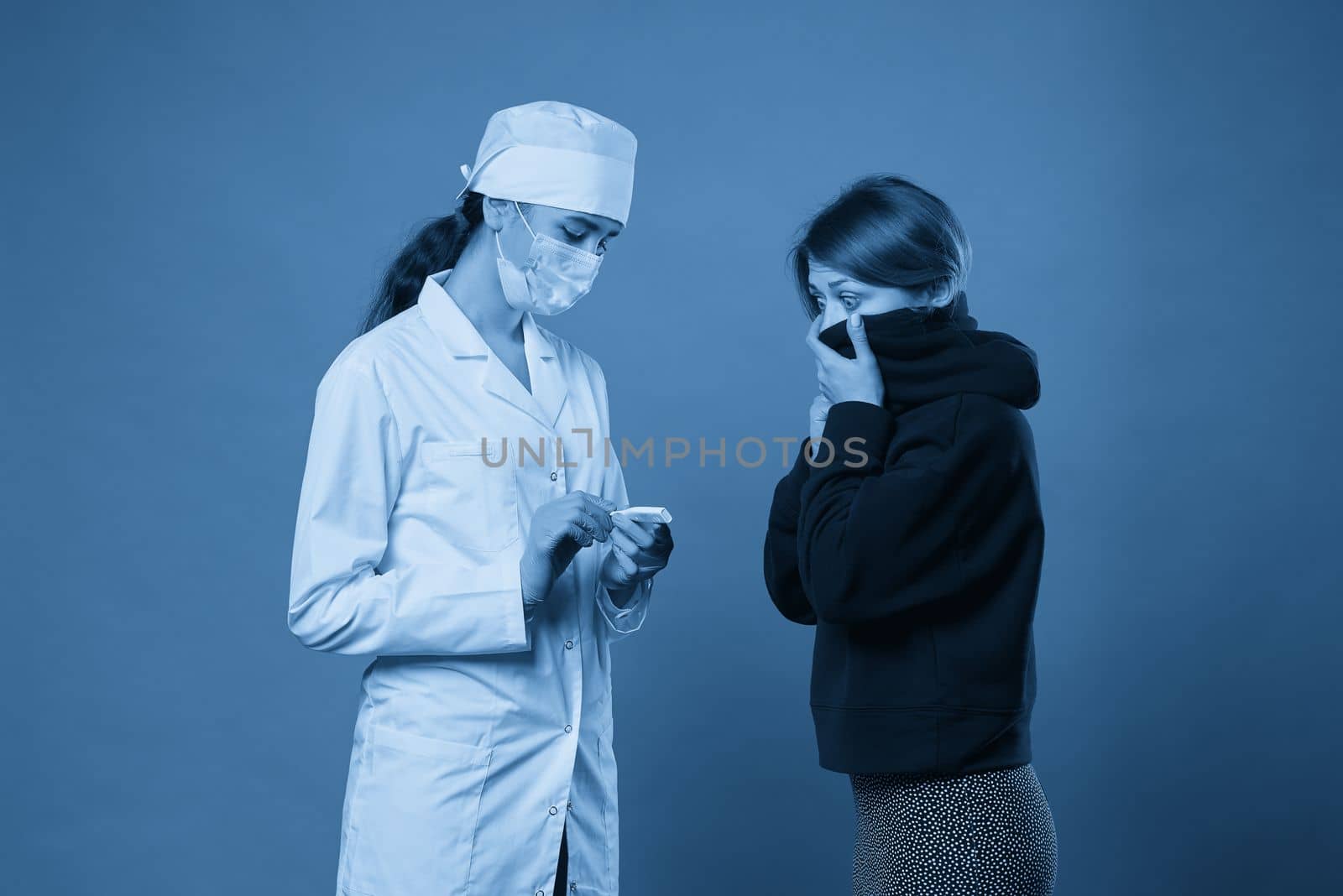 Young doctor measuring temperature of a patient with thermometer, studio shot on blue background by Mariakray