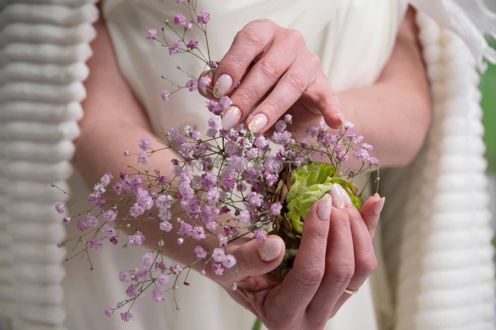wedding manicure for the bride, a girl in a wedding dress holds a bouquet of ronunculus and pink gypsophila in her hands. High quality photo