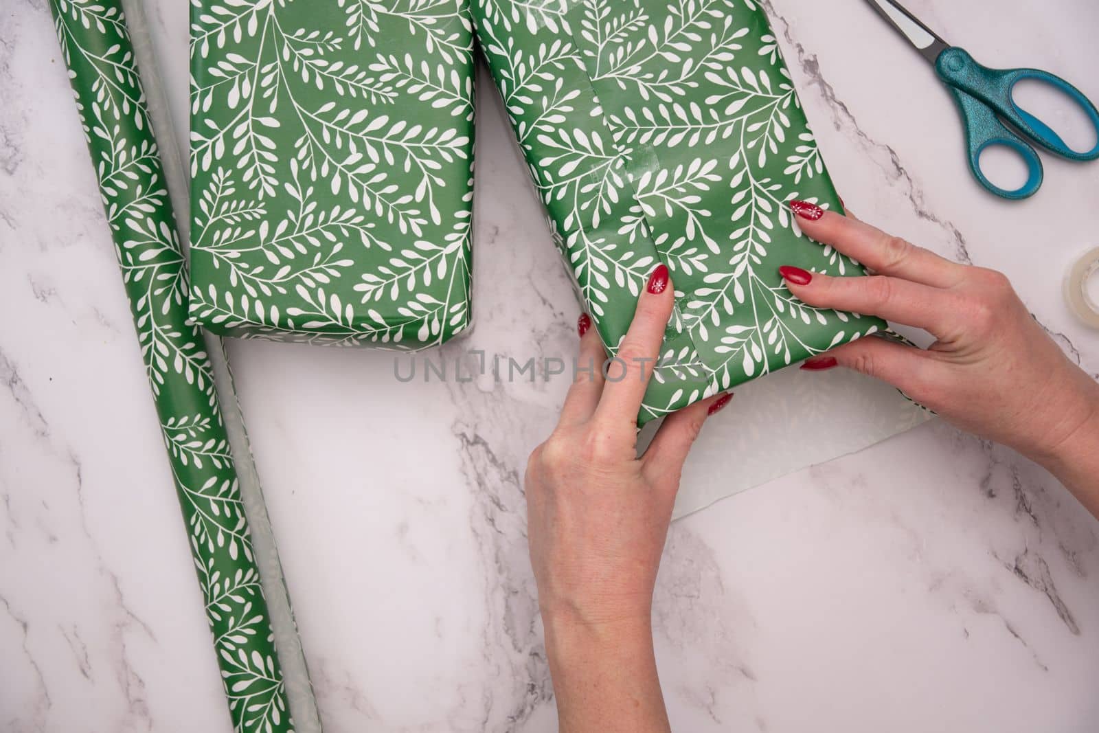 woman's hands with red christmas manicure wrap gifts in green wrapping paper. High quality photo