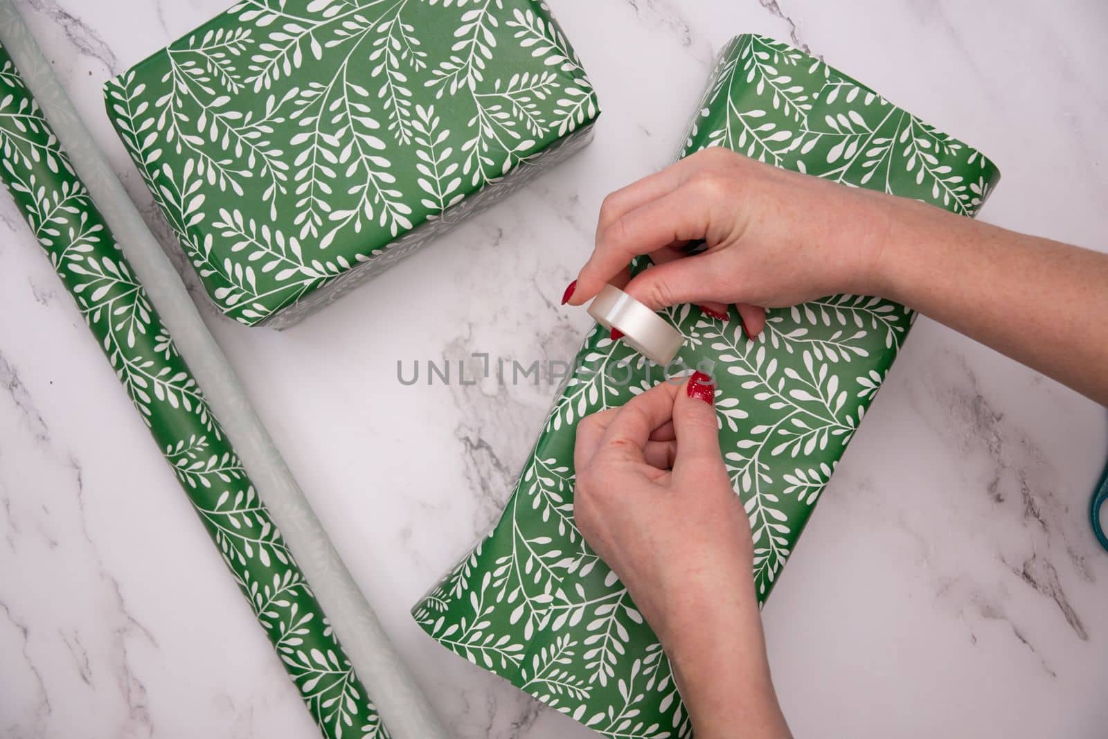 woman's hands with red christmas manicure wrap gifts in green wrapping paper. High quality photo