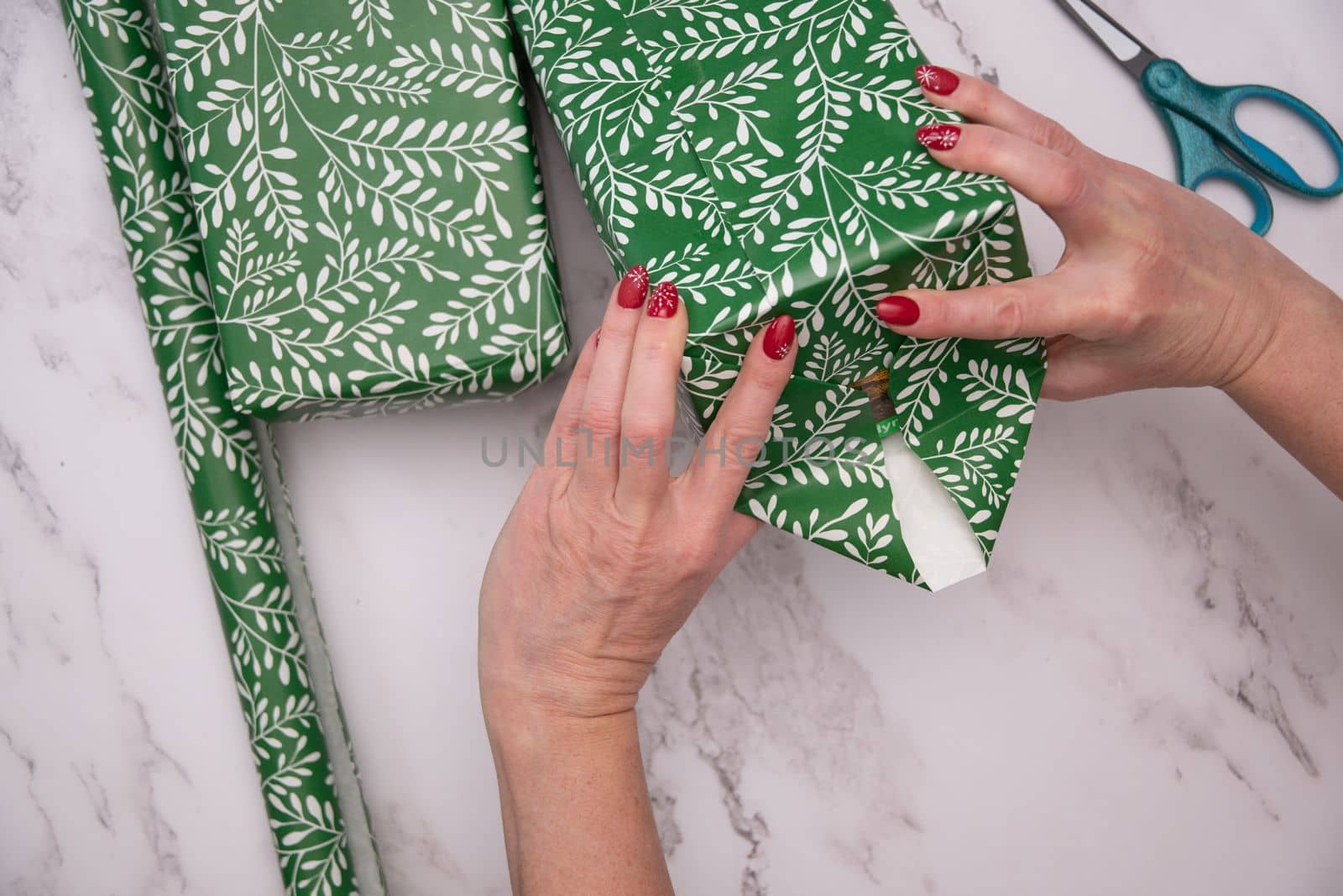 woman's hands with red christmas manicure wrap gifts in green wrapping paper. High quality photo