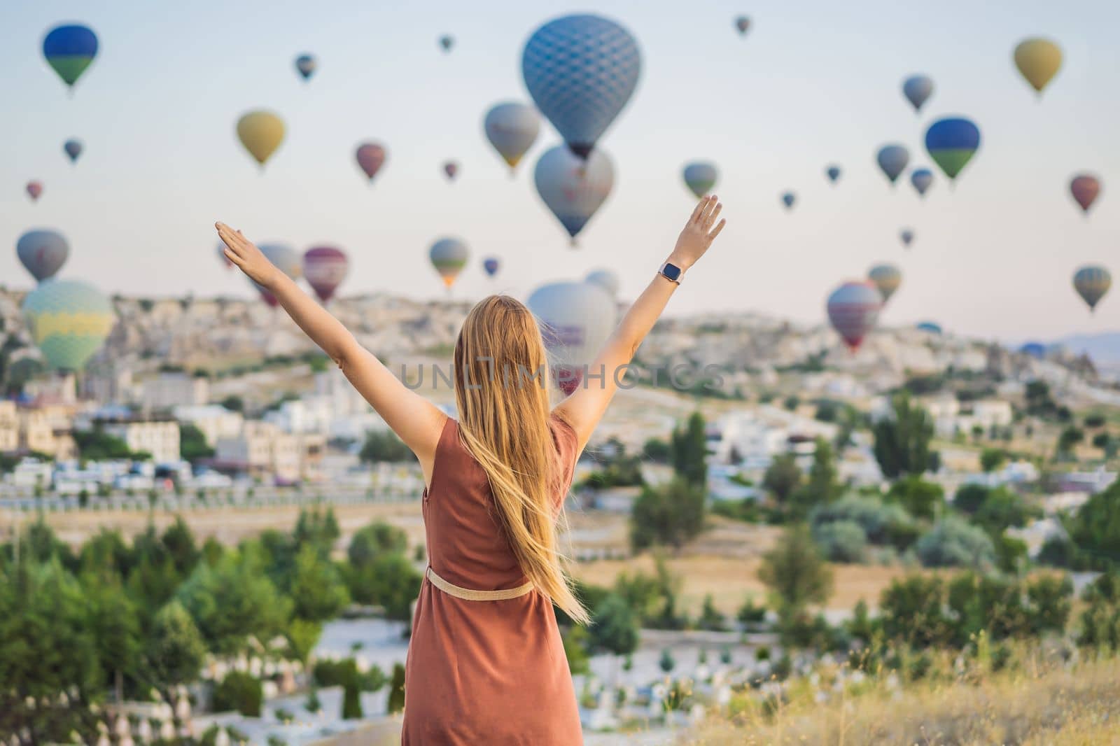Tourist woman looking at hot air balloons in Cappadocia, Turkey. Happy Travel in Turkey concept. Woman on a mountain top enjoying wonderful view.