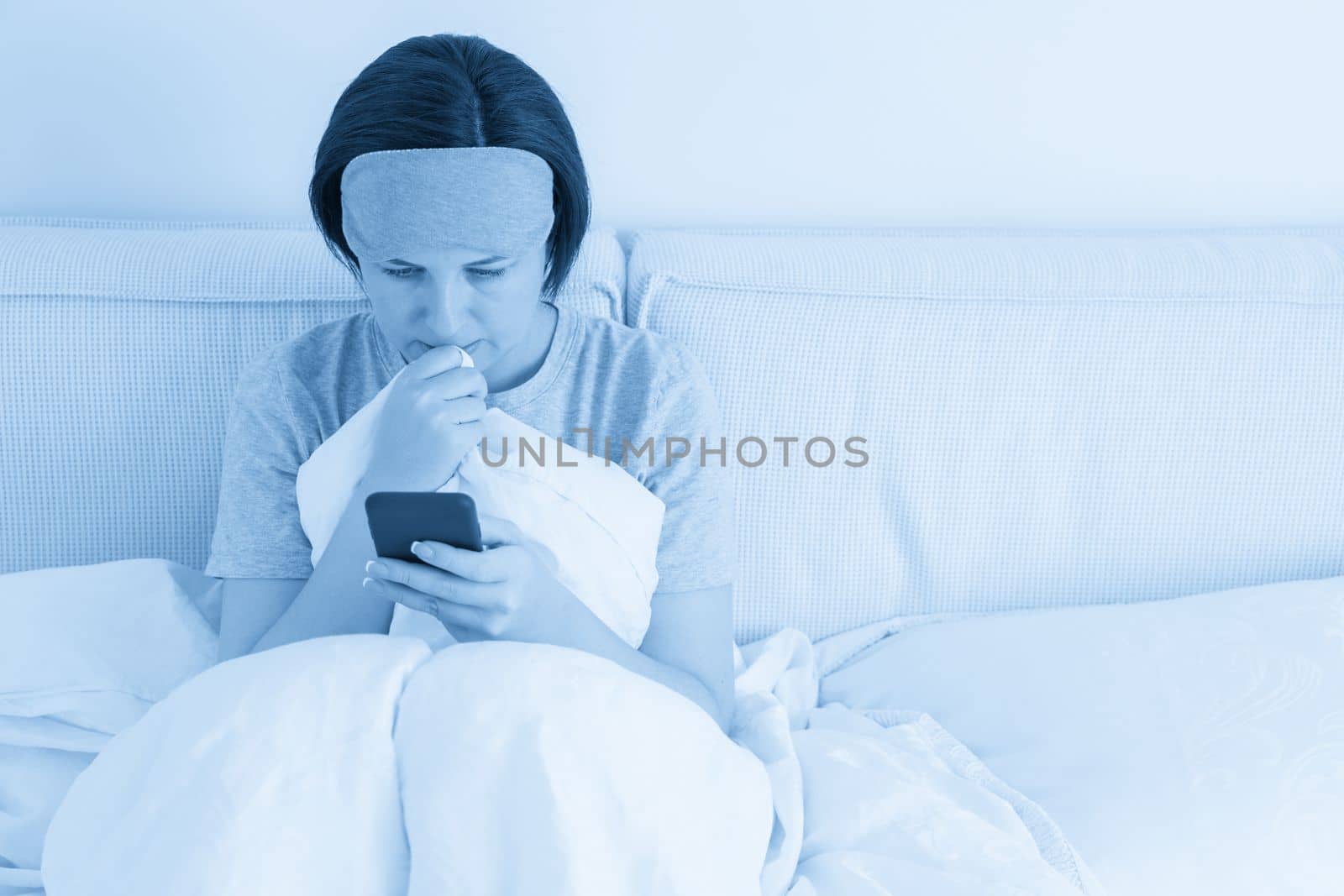 Woman using smartphone as she sits in bed covered with a duvet