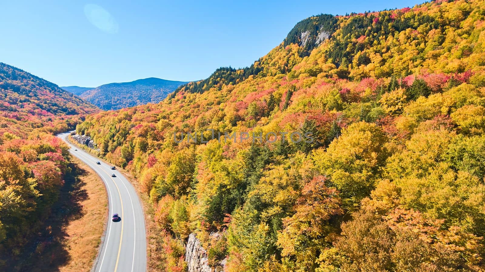 Aerial view of road tucked into New Hampshire mountains covered in peak fall foliage by njproductions