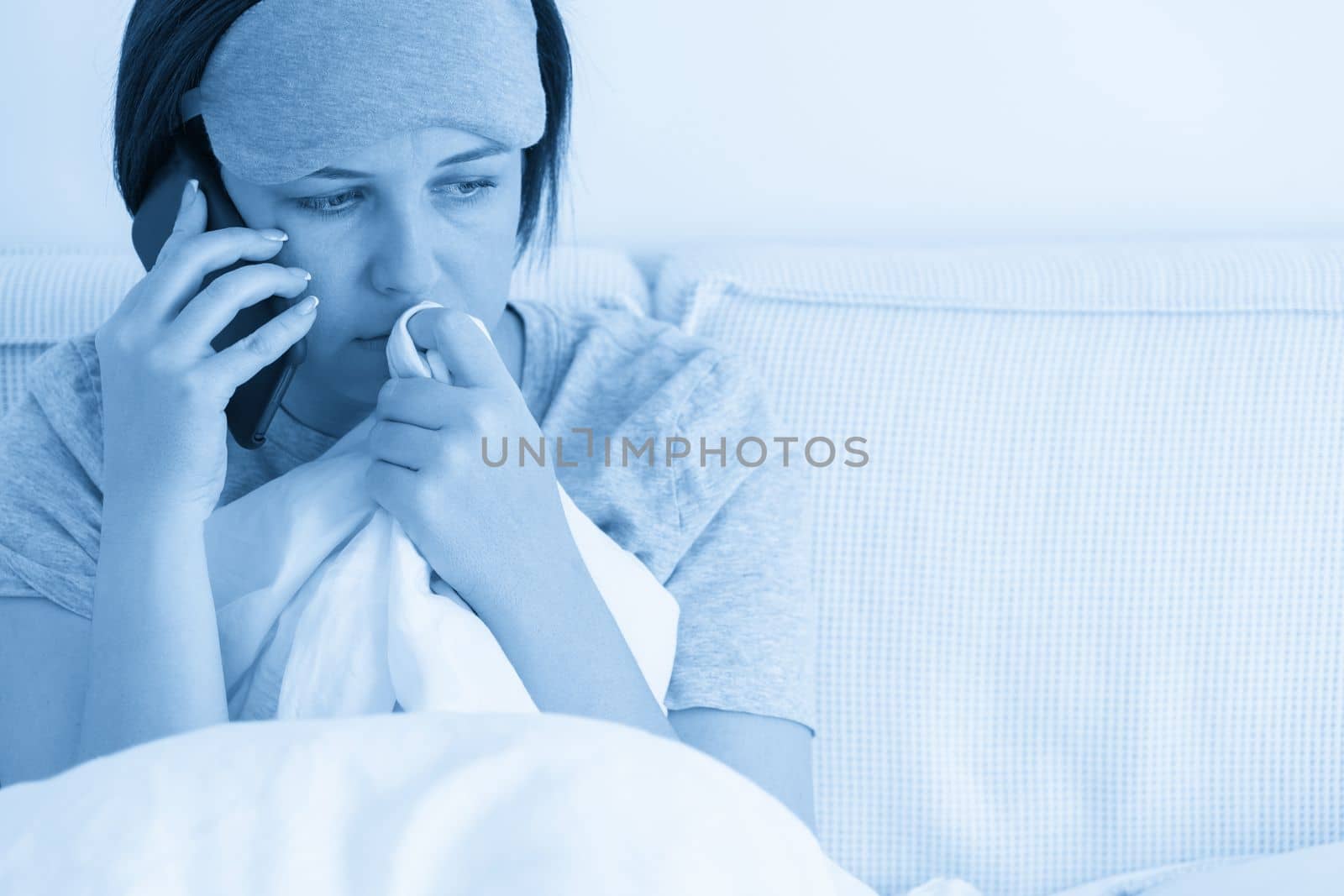 Upset Woman using smartphone as she sits in bed covered with a duvet