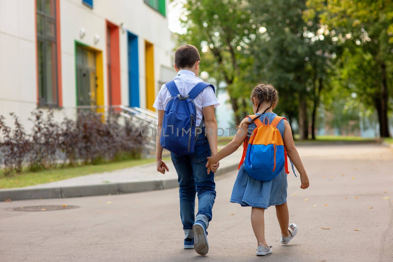 two schoolchildren, a little girl and a boy, brother and sister with backpacks hold hands go to school in the morning on a sunny summer day. Close up. Mock up