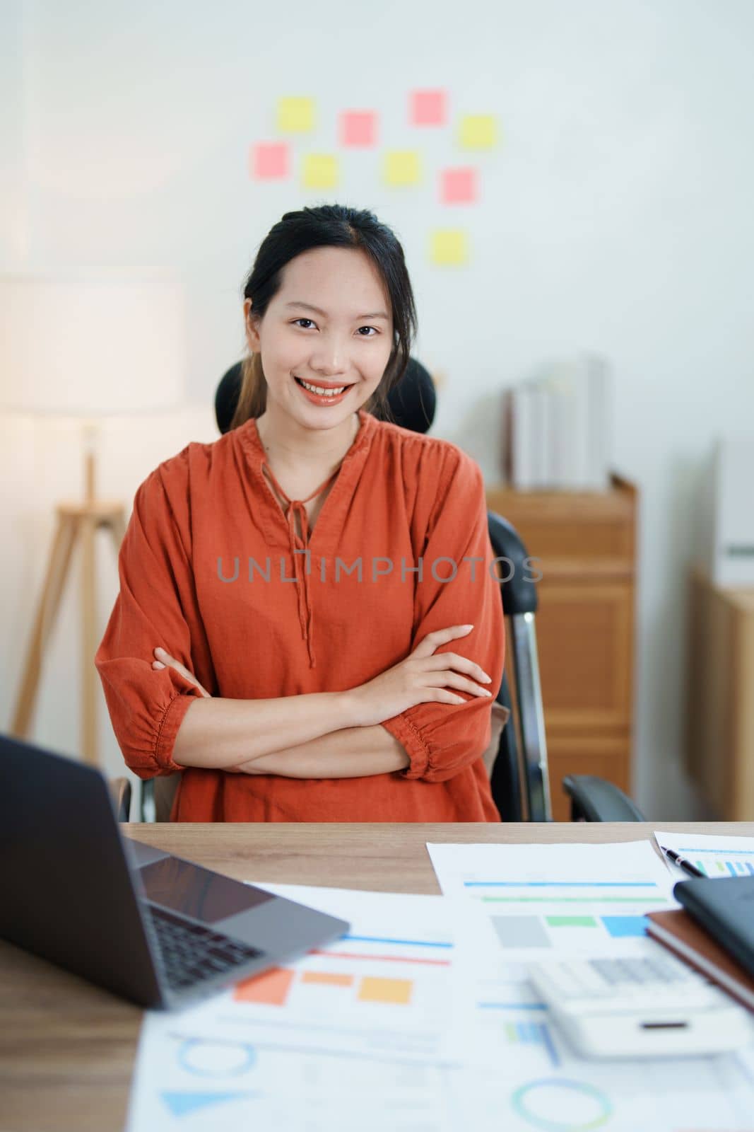 Portrait of a woman business owner showing a happy smiling face as he has successfully invested her business using computers and financial budget documents at work by Manastrong