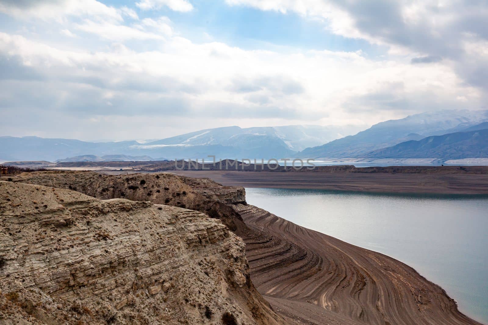 A beautiful reservoir in the mountains. Low water level, drought and beautiful patterns are visible along the banks. A red pleasure boat is standing by the shore