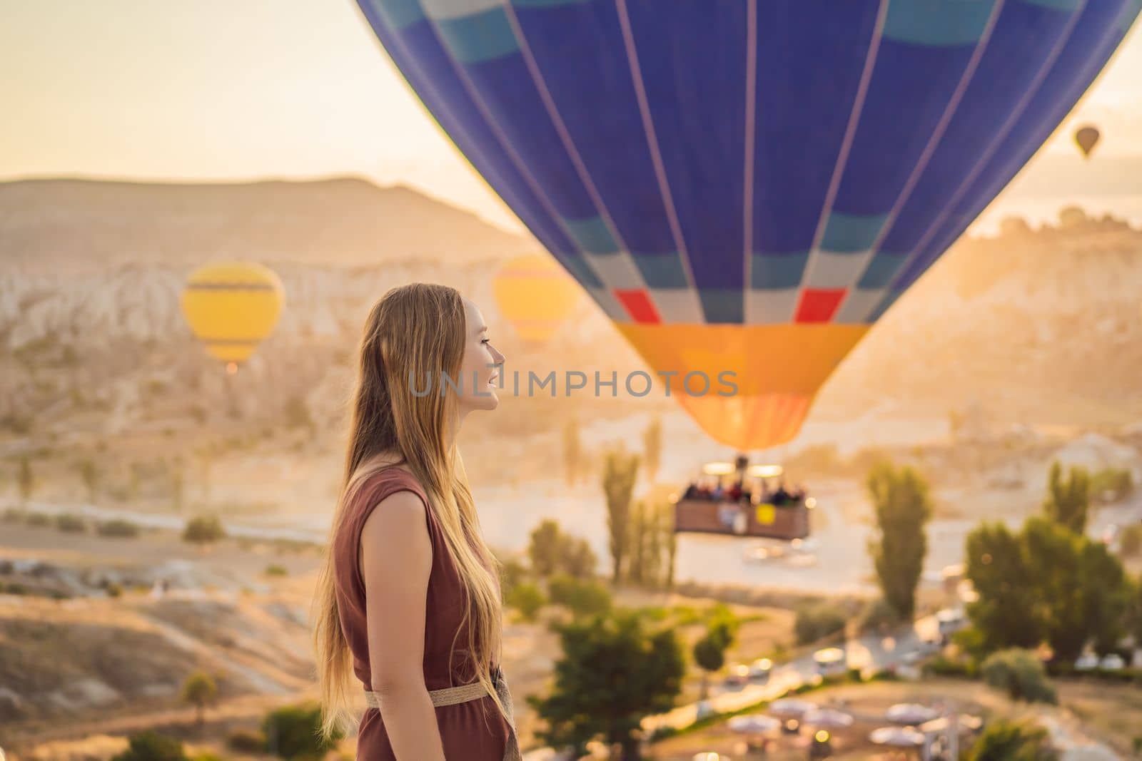 Tourist woman looking at hot air balloons in Cappadocia, Turkey. Happy Travel in Turkey concept. Woman on a mountain top enjoying wonderful view.