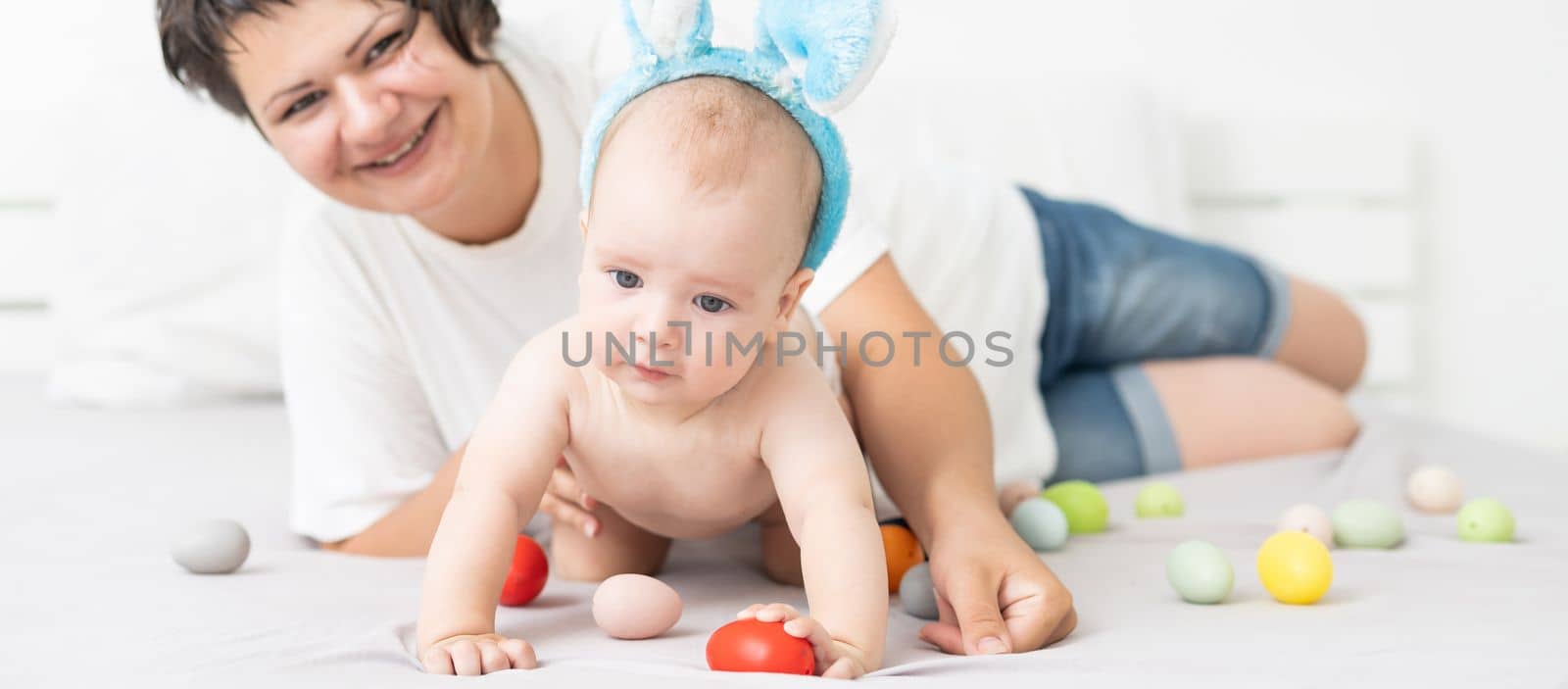 Mother and child with colorful eggs. Mom and baby with bunny ears. Parent and kid play indoors in spring. Family celebrating Easter.