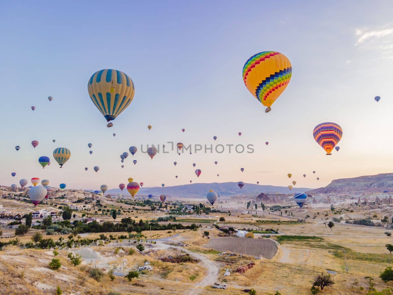 Colorful hot air balloons flying over at fairy chimneys valley in Nevsehir, Goreme, Cappadocia Turkey. Spectacular panoramic drone view of the underground city and ballooning tourism. High quality.