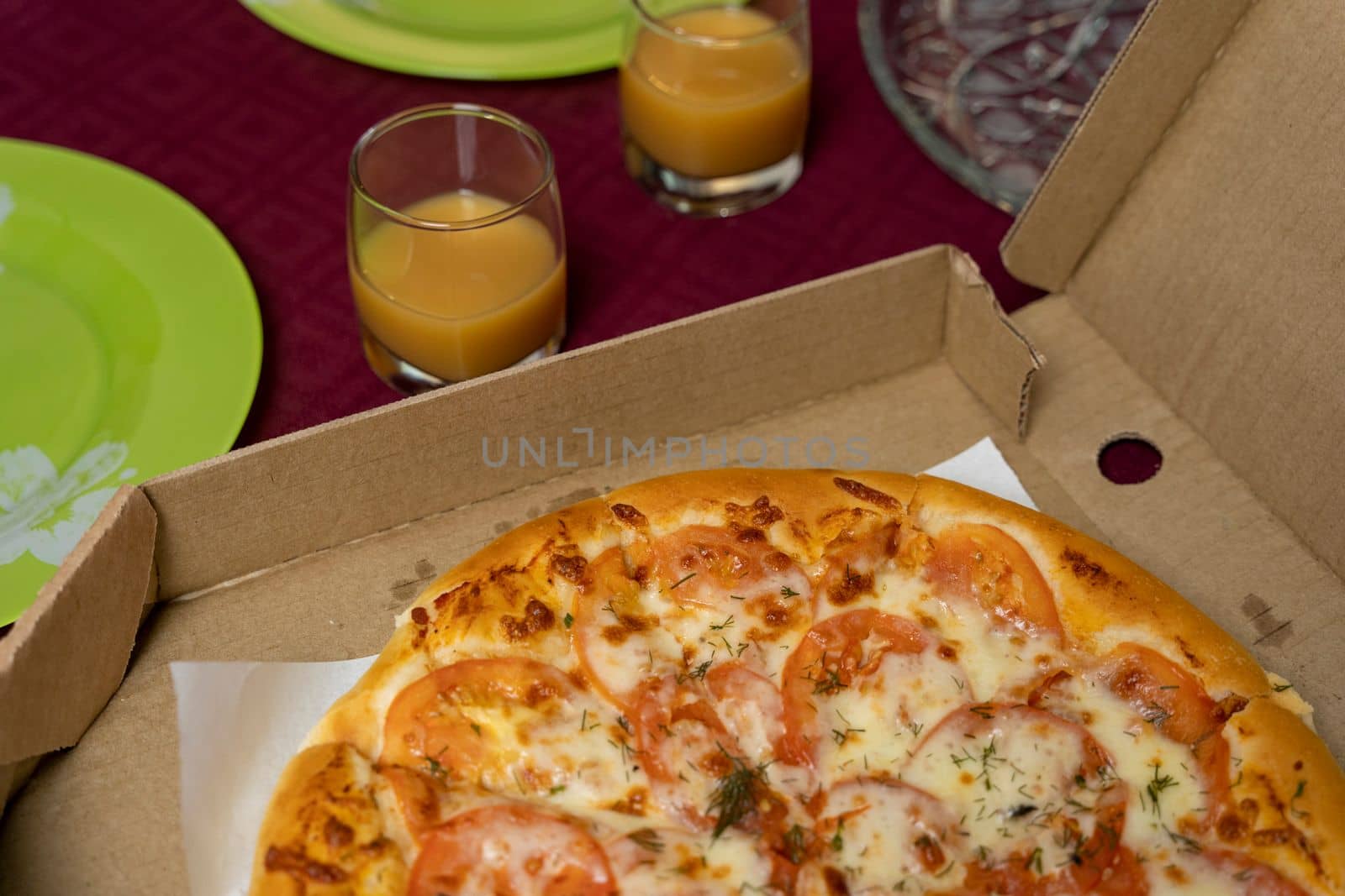 Hot pizza in a cardboard box on the table, top view. Celebration of the event. glasses with orange juice, plates