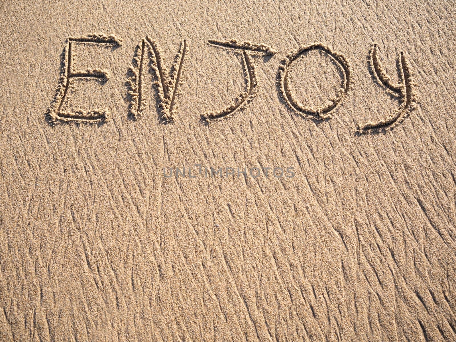 Enjoy word is written on the beach sand with copy space by papatonic