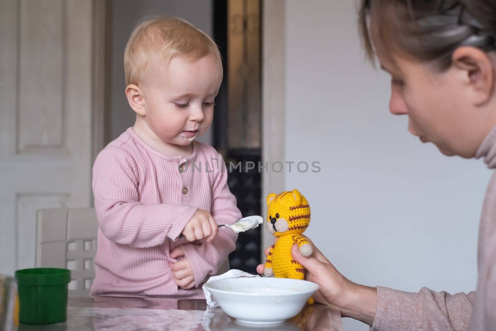 adorable little girl feeding tiger toy with spoon during breakfast