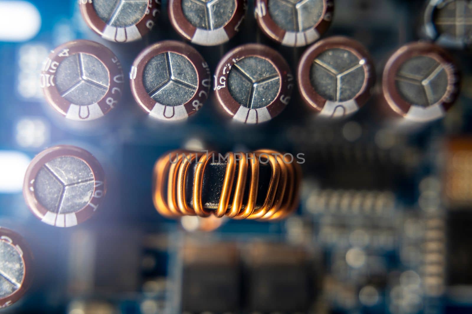 Background of various electronic components on a blue printed circuit board in close-up. Ferrite core of a toroidal inductor wrapped with copper wire, resistors and capacitors on a blue printed circuit board. The concept of electro and microprocessor technologies. Selective focus