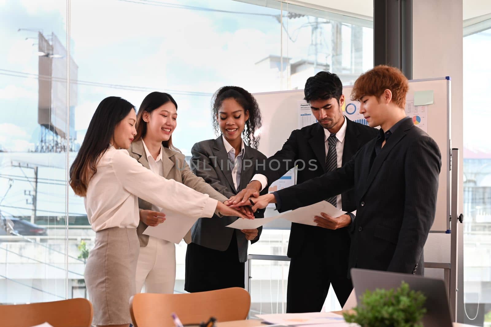 Group of young businesspeople putting hands together, showing support and unity during meeting in corporate meeting.