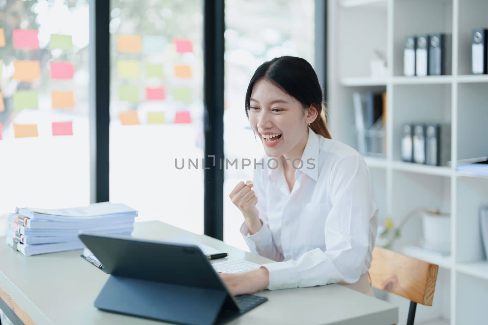 Portrait of a woman business owner showing a happy smiling face as he has successfully invested her business using computers and financial budget documents at work by Manastrong