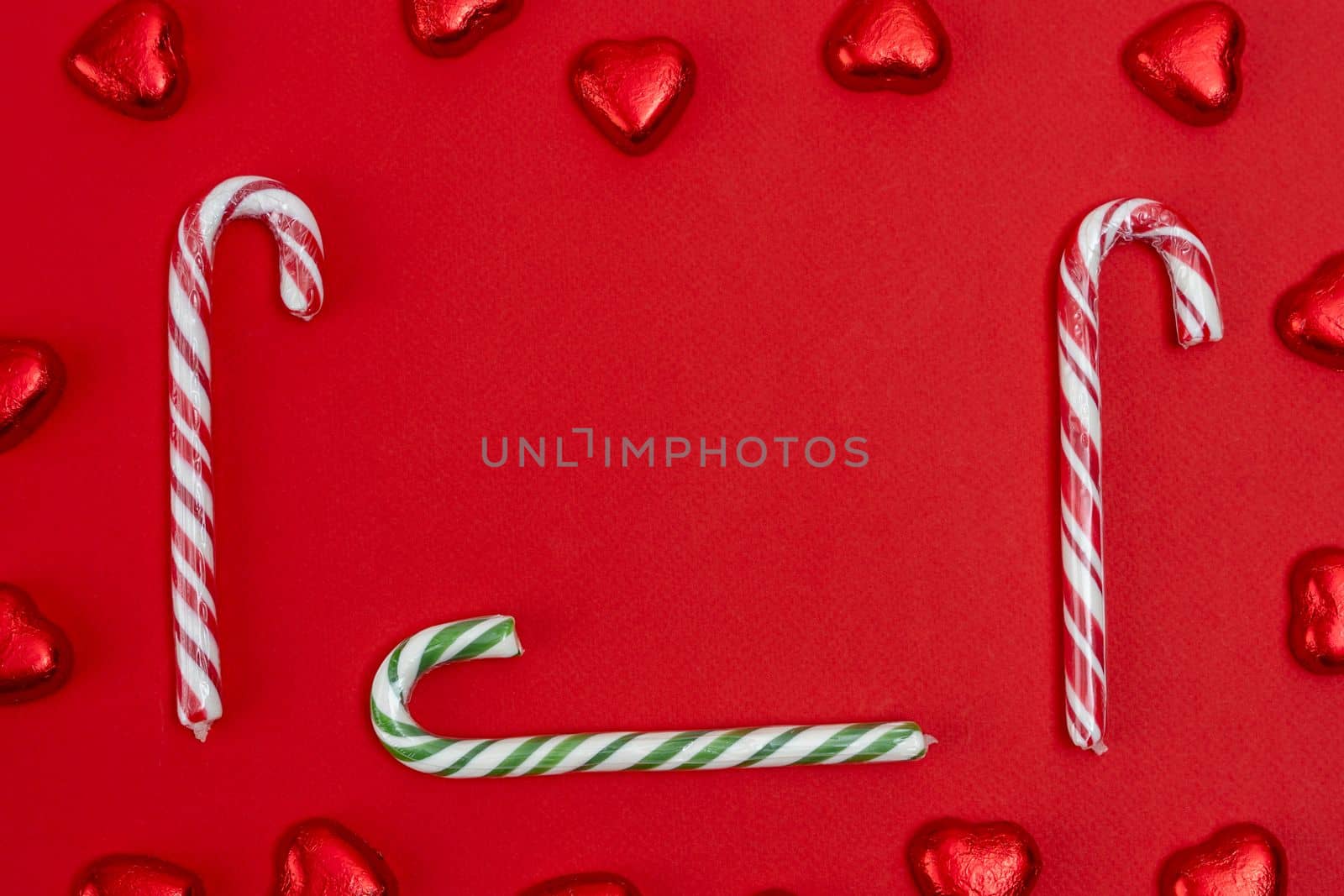 red festive Christmas background with candy in the shape of hearts wrapped in shiny foil and candy in the shape of a caramel cane