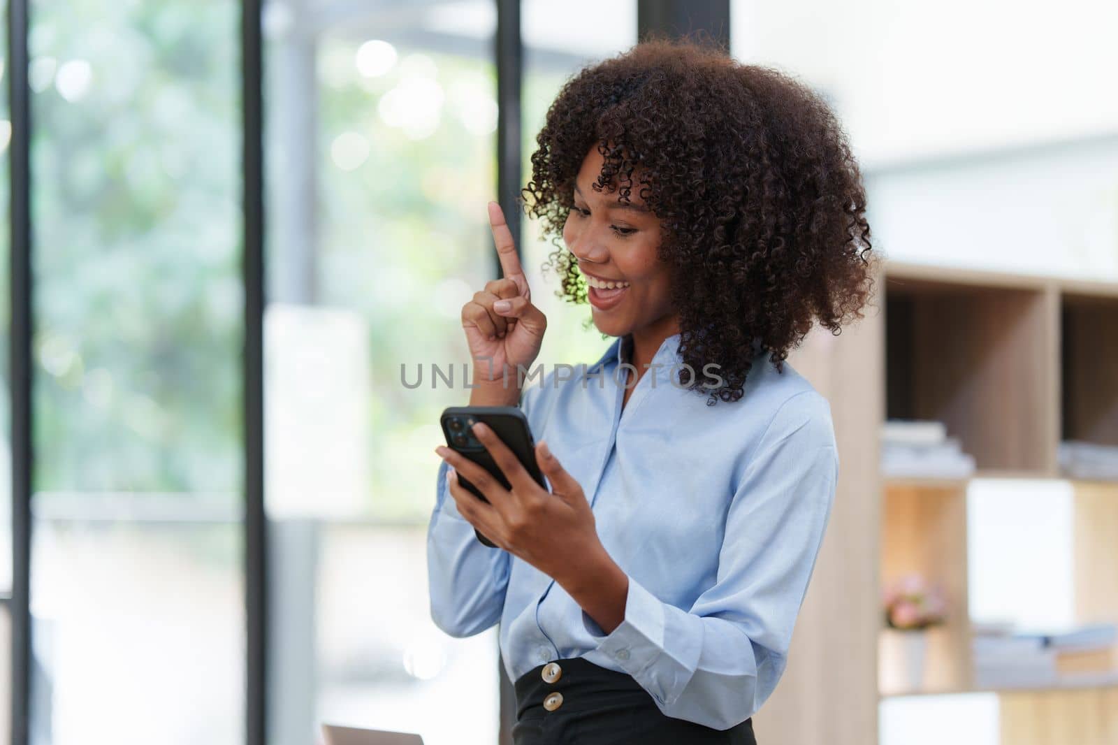 Business black woman having phone conversation with client in office. African american young woman using smart phone by itchaznong