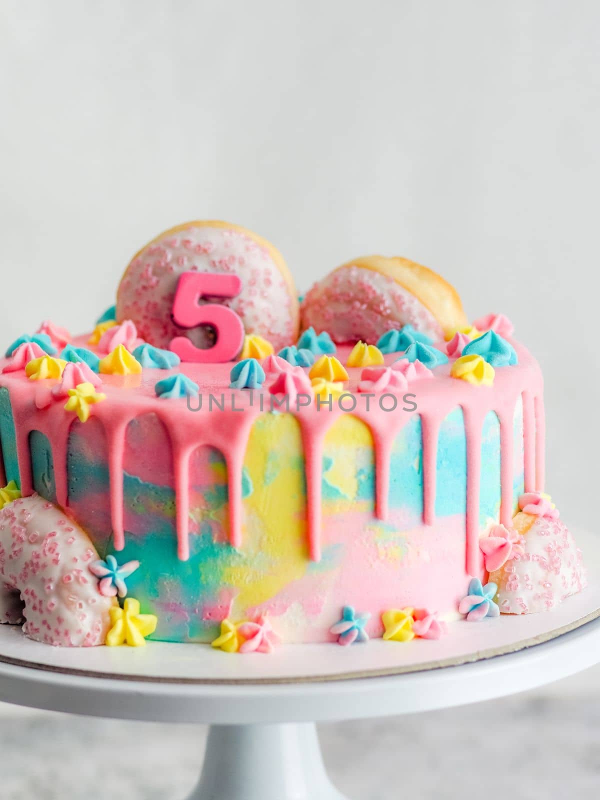 Close up of pink frosted dripping cake with donut and plastel brushed royal star sprinkles insolated on white studio shot
