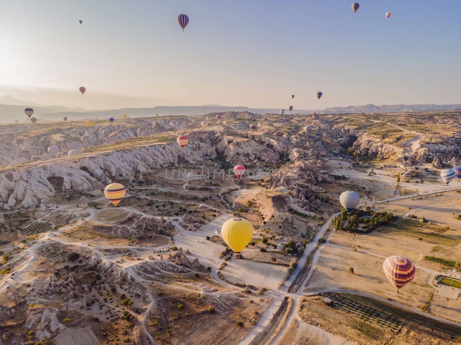 Colorful hot air balloons flying over at fairy chimneys valley in Nevsehir, Goreme, Cappadocia Turkey. Spectacular panoramic drone view of the underground city and ballooning tourism. High quality by galitskaya