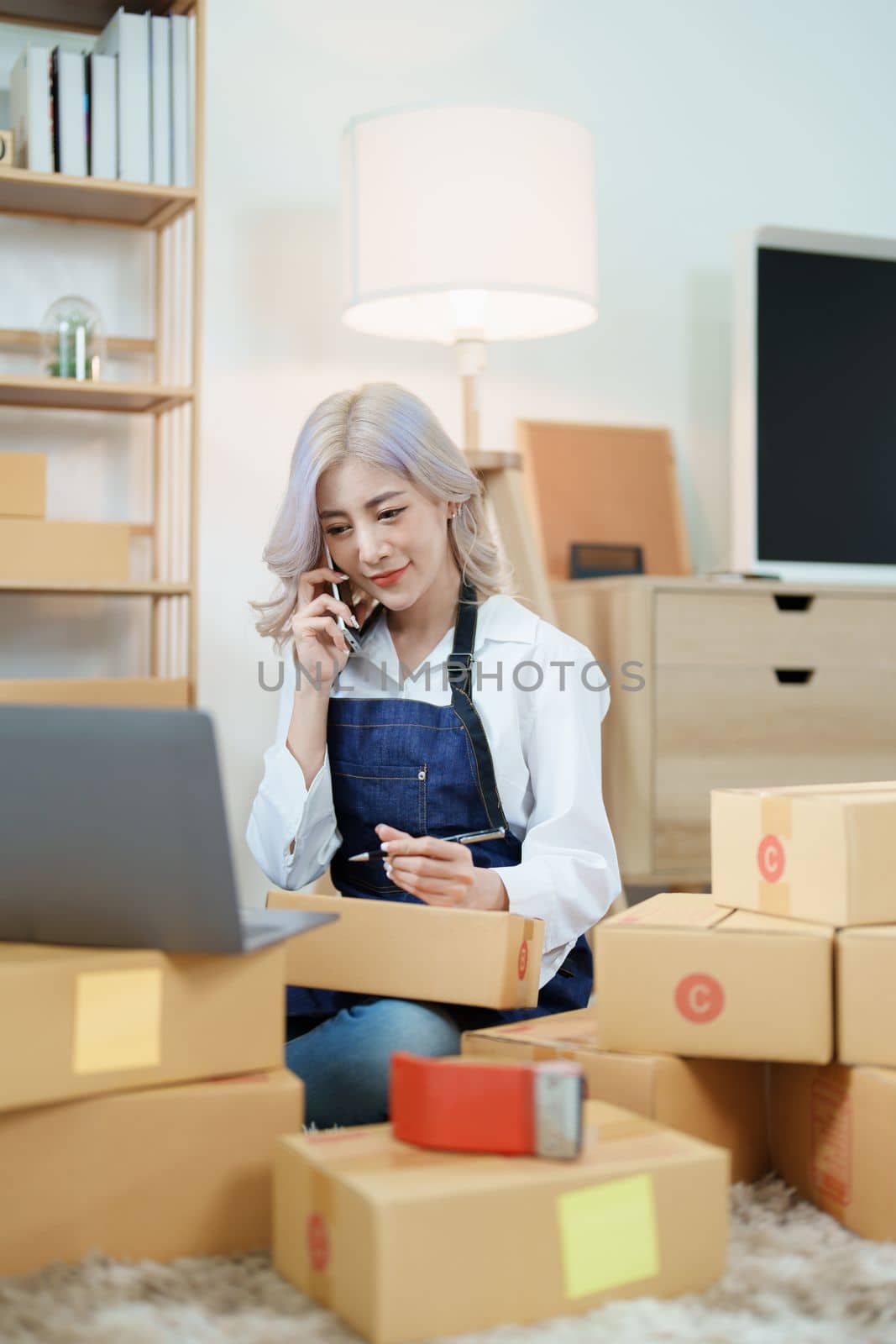 Starting small business entrepreneur of independent Asian woman smiling using computer laptop with cheerful success of online marketing package box items and SME delivery concept.