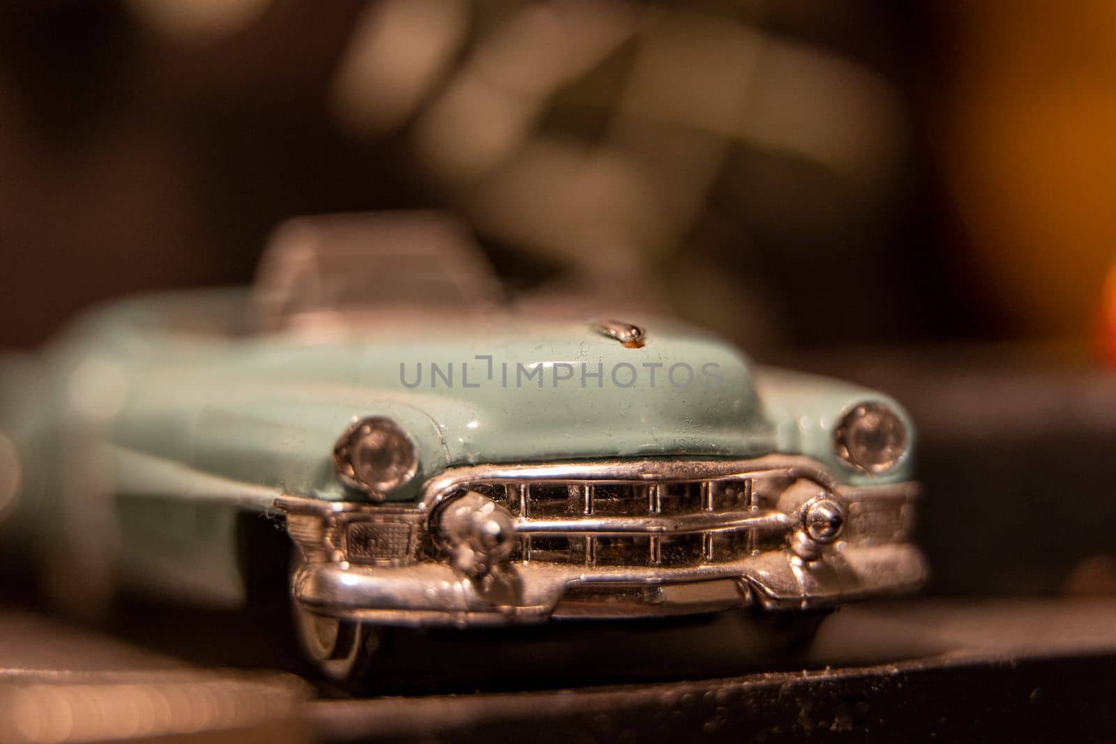 A toy model of a beautiful vintage car with a chrome bumper and radiator grille. Close-up of a turquoise vintage stylish car. Shiny radiator grill. Old retro or vintage car. blurred image