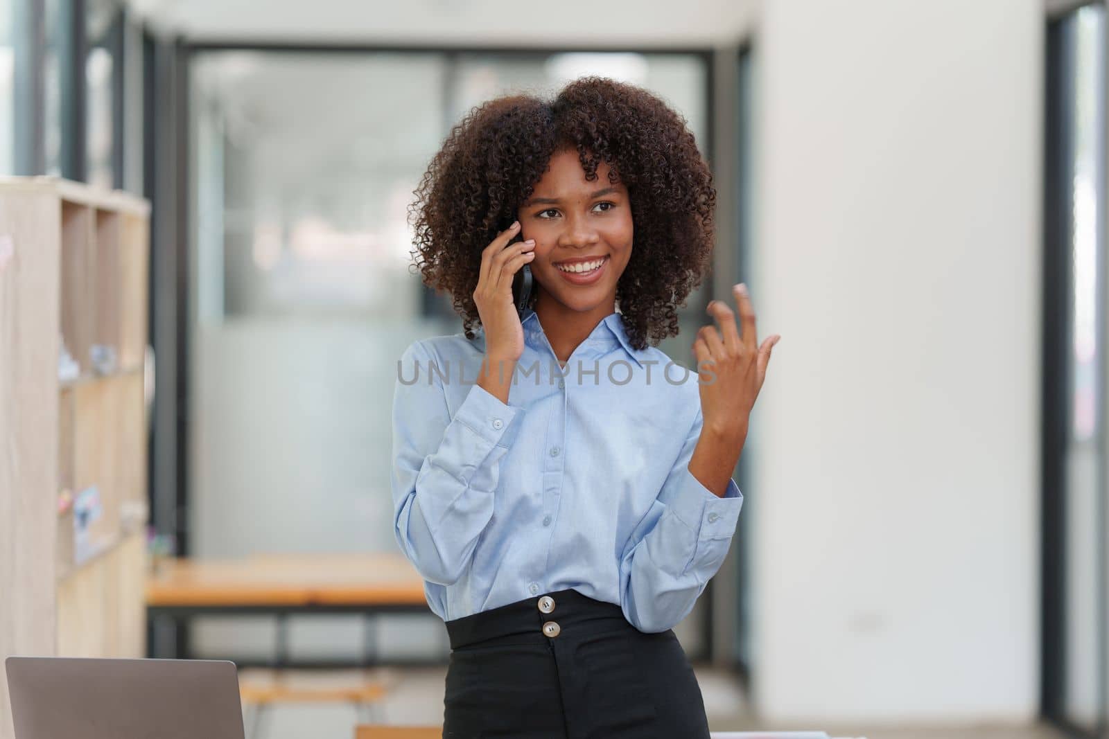 Business black woman having phone conversation with client in office. African american young woman using smart phone by itchaznong