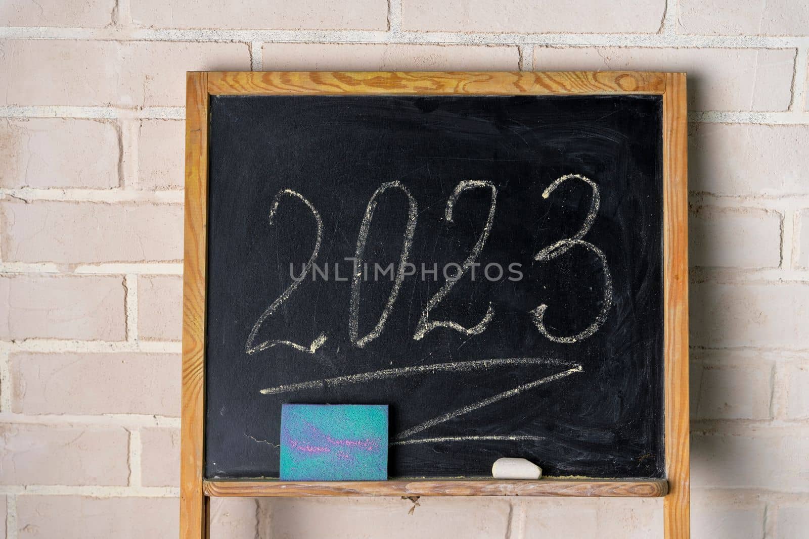 a black slate decorated with with a piece of chalk and a sponge. The year 2023 is written in chalk on the blackboard. Happy New Year. 2023. Number written in chalk on a school board