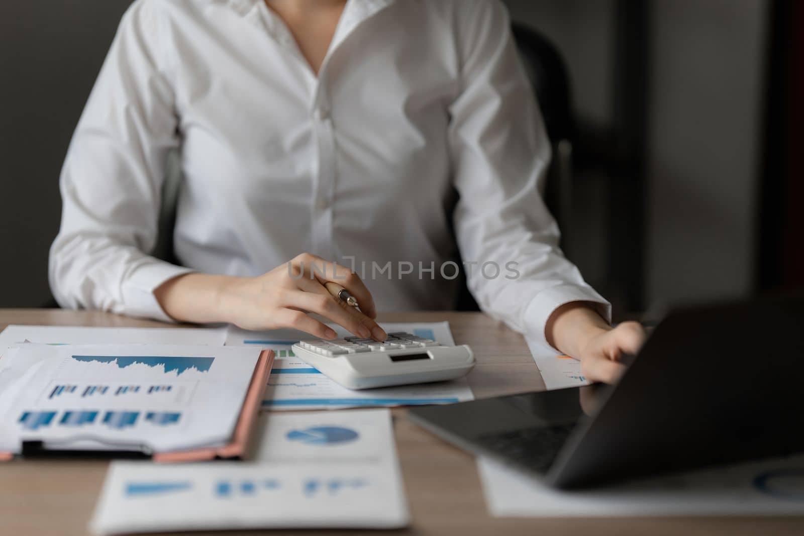 Close up Business woman using calculator and laptop for do math finance on wooden desk in office and business working background, tax, accounting, statistics and analytic research concept by itchaznong