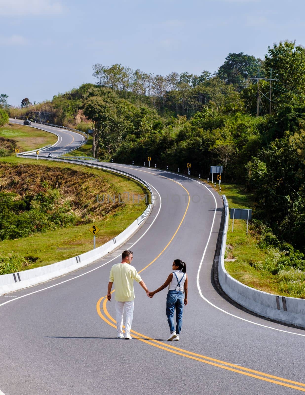 A couple walking at a curved road in the mountains of Nan Thailand, Road nr 3 country road  by fokkebok