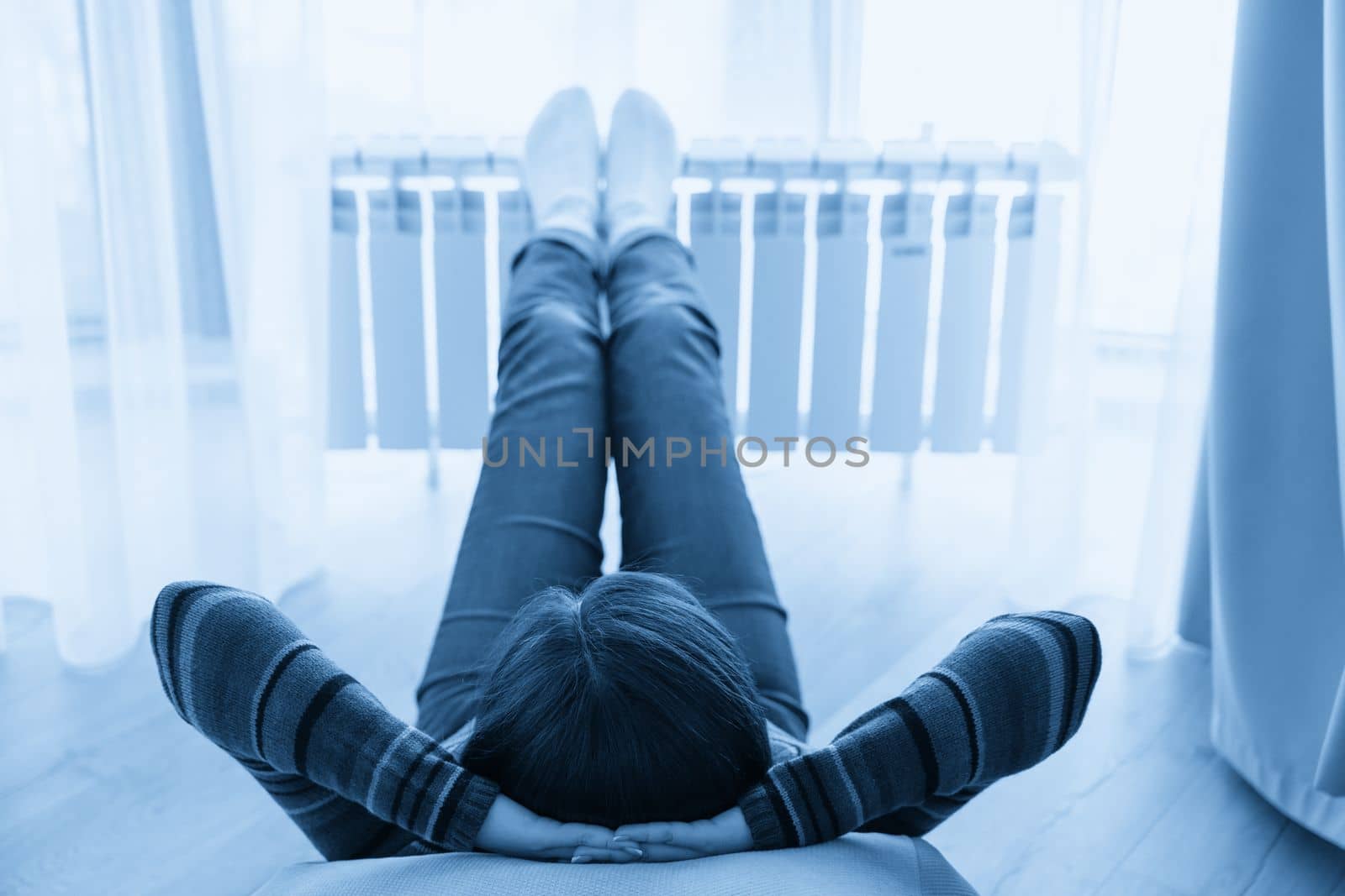 Woman laying on floor with feet raised up on radiator for warming up by Mariakray